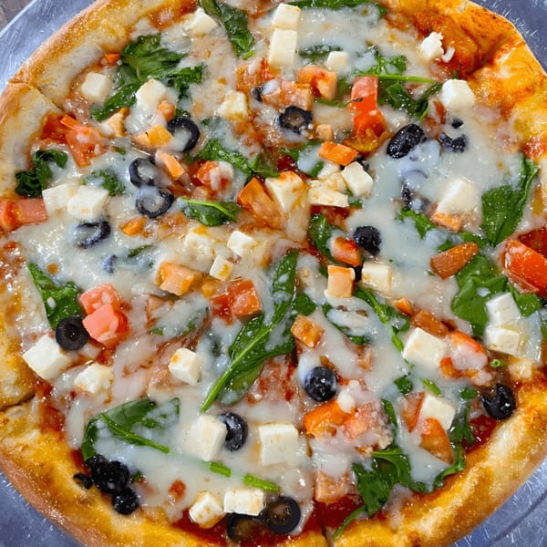 Close-up of a Casa Express pizza with melted cheese, spinach, tomatoes, olives, and feta.