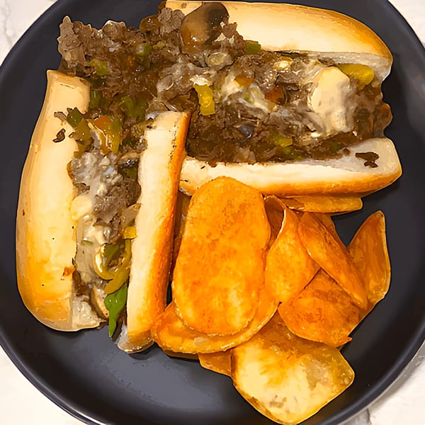 A Casa Express Italian cheesesteak sandwich with peppers and onions, served with potato chips.