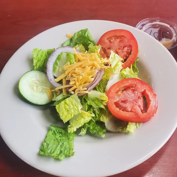 A fresh side salad with lettuce, tomatoes, cucumbers, red onion, and shredded cheese.