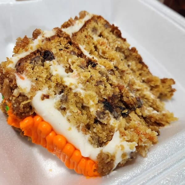 A slice of carrot cake with white frosting and orange icing, served on a white plate.