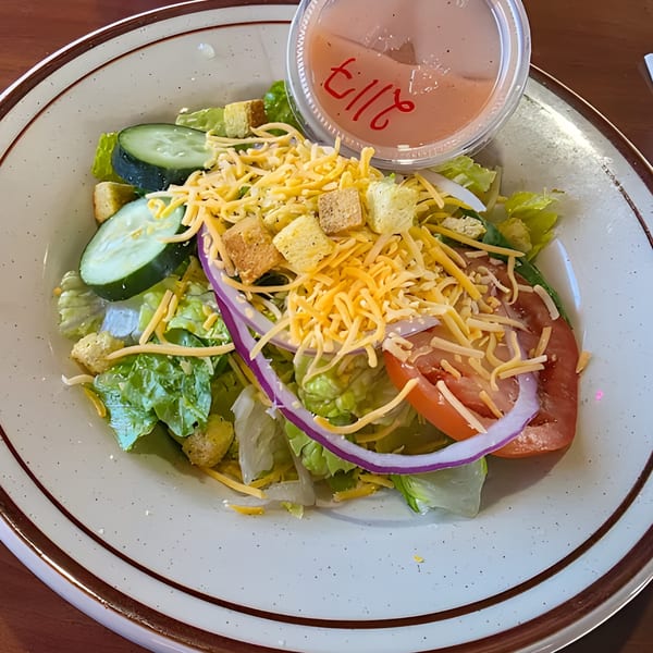 A fresh side salad with lettuce, cucumbers, tomatoes, red onion, shredded cheese, and croutons.
