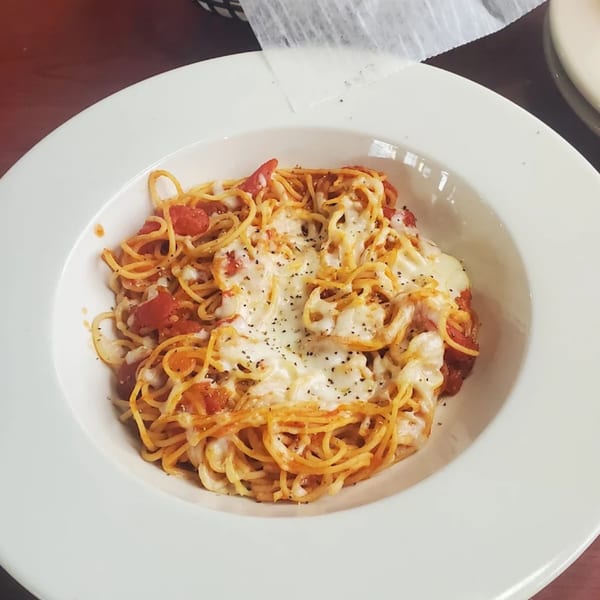 A white bowl of Casa Express spaghetti with melted cheese, tomato sauce, and black pepper.