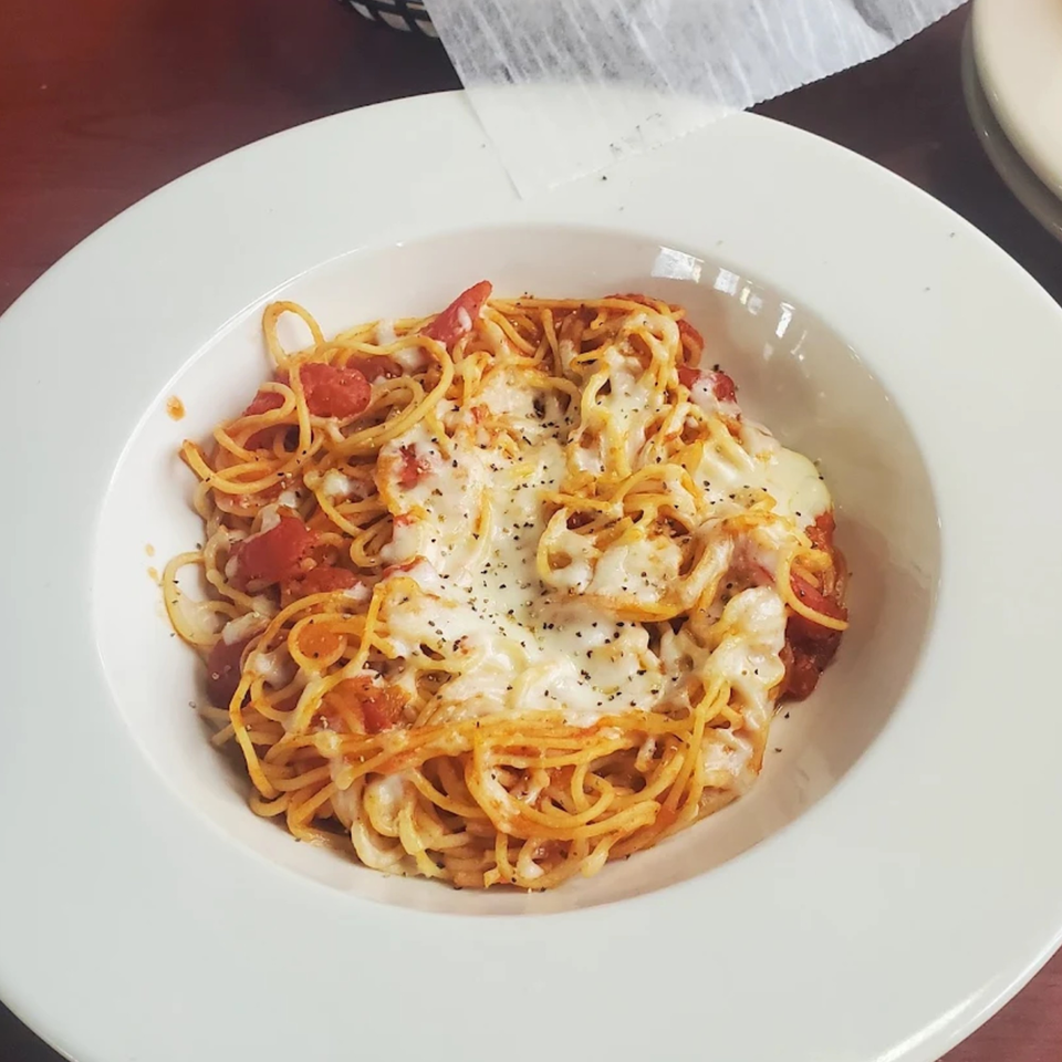 A white bowl of Casa Express spaghetti with melted cheese, tomato sauce, and black pepper.