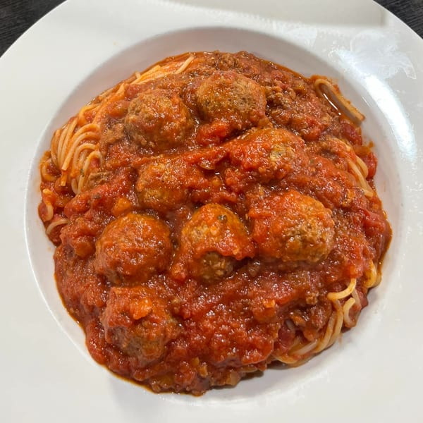 Spaghetti with meatballs and rich red marinara sauce in a white bowl from Casa Express.